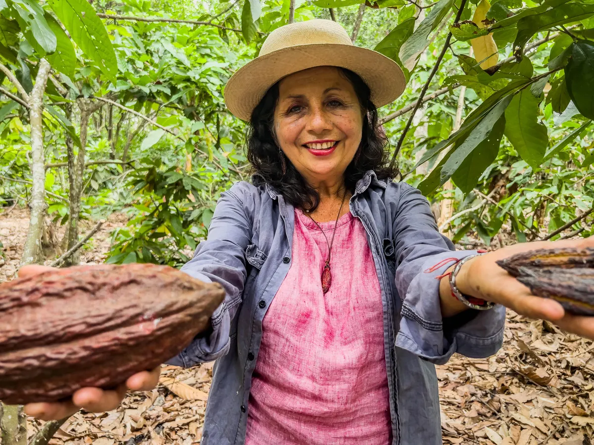 Productora sonriente muestra dos mazorcas de cacao en una plantación.
